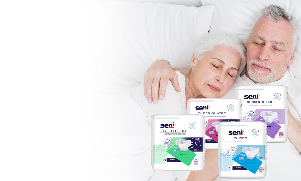 Ein Paar liegt schlafend auf einem Bett, umarmt. Im Vordergrund sind verschiedene Verpackungen von Inkontinenzprodukten der Marke Seni sichtbar, die unterschiedliche Typen und Größen präsentieren.